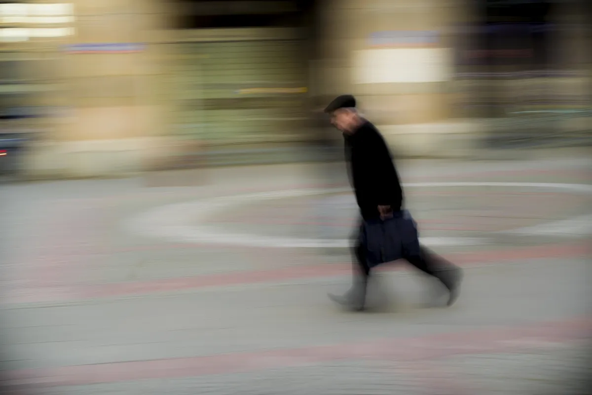 Older man walking with a rolling suitcase in motion blur